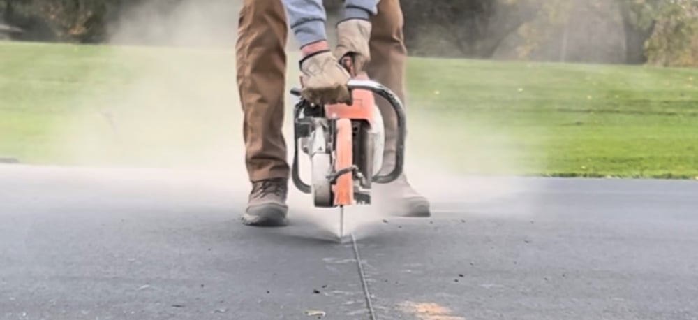 A machine cutting into an asphalt driveway to bury wire.