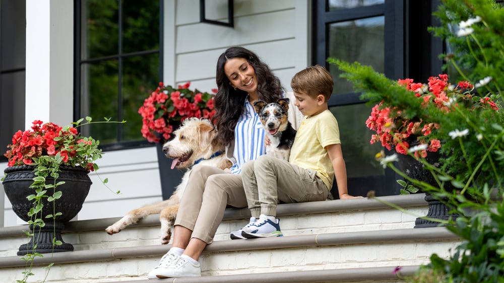 Mother and son sit outside on the porch with their two dogs 