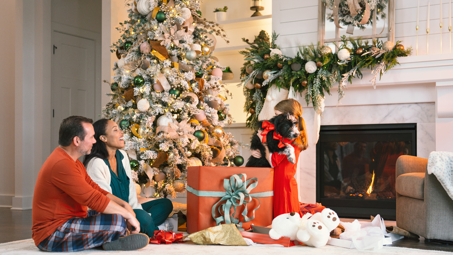 Family celebrating the holidays with their dog next to the Christmas tree opening gifts